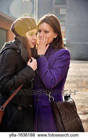 Young women whispering in friend ear outdoors View Large Photo Image Stock Photo - Young women whispering in friend ear outdoors. Fotosearch