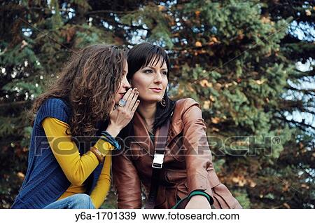 Young women whispering in friend ear outdoors View Large Photo Image Stock Photo - Young women whispering in friend ear outdoors. Fotosearch