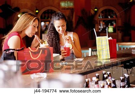 Young women with shopping bags, having a drink in a bar View Large Photo Image Picture - Young women with shopping bags, having a drink in a bar. Fotosearch