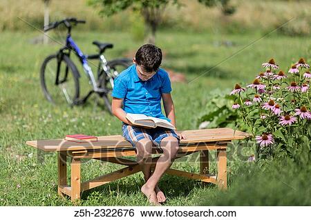 Stock Photograph - A boy of twelve years in the garden on a wood bench with a book.. Fotosearch