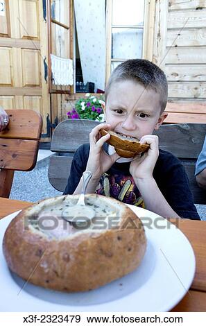 Stock Photo - Boy age 8 eating the cover from polish bread soup {zupa chlebowa) at an outdoor restaurant. Spala Central Poland.. Fotosearch