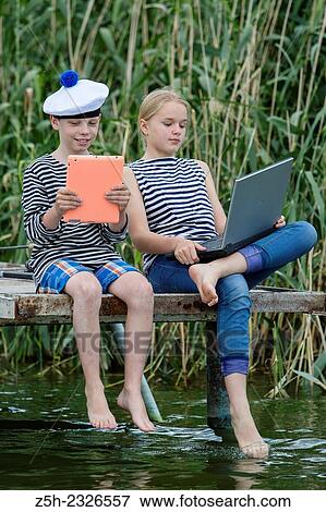 Stock Photo - Boy and girl of twelve years in a sailor uniform with a laptop on the dock.. Fotosearch