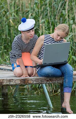 Stock Photo - Boy and girl of twelve years in a sailor uniform with a laptop on the dock.. Fotosearch