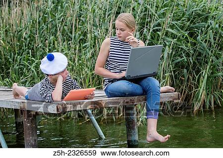 Stock Photo - Boy and girl of twelve years in a sailor uniform with a laptop on the dock.. Fotosearch