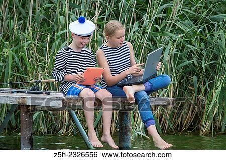 Stock Photograph - Boy and girl of twelve years in a sailor uniform with a laptop on the dock.. Fotosearch