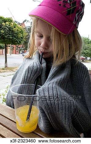Chilly girl age 6 wrapped in sweater while sipping orange juice thru a straw at a sidewalk cafe. Rawa Mazowiecka Central Poland. View Large Photo Image Stock Image - Chilly girl age 6 wrapped in sweater while sipping orange juice thru a straw at a sidewalk cafe. Rawa Mazowiecka Central Poland.. Fotosearch