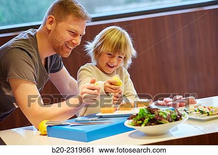 Stock Image - Family in the kitchen. Father and son. Healthy eating. Healthy growth. Taking lemon fish.. Fotosearch