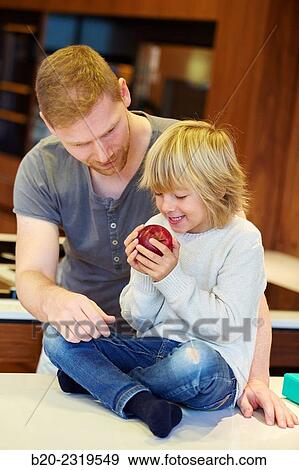 Stock Photo - Family in the kitchen. Father and son. Healthy eating. Healthy growth. Apple.. Fotosearch