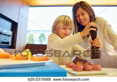 Stock Photo - Family in the kitchen. Mother and son. Healthy eating. Healthy growth. Season the fish.. Fotosearch