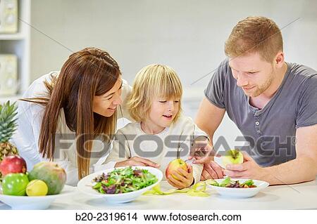 Picture - Family in the kitchen. Parents and son. Healthy eating. Healthy growth. Eating an apple.. Fotosearch