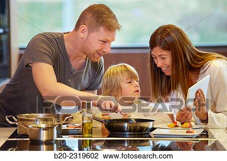 Stock Image - Family in the kitchen. Parents and son cooking and looking recipe on a tablet. Healthy eating. Healthy growth.. Fotosearch