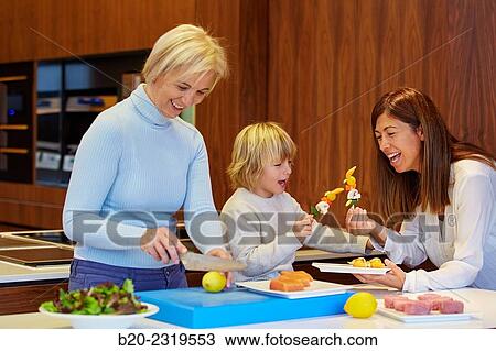 Stock Image - Family in the kitchen. Three generations. Healthy eating. Healthy growth. Cooking fish and vegetable skewer.. Fotosearch