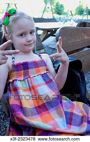 Stock Photo - Girl age 6 wearing a madras plaid dress giving a sign while waiting for dinner at an outdoor restaurant. Spala Central Poland.. Fotosearch