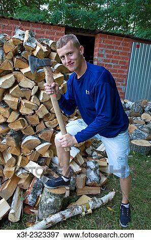 Stock Photo - Polish teen wood chopper holding ax beside large pile of split wood. Zawady Central Poland.. Fotosearch