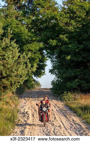 Stock Photo - Polish teenager driving motorcycle down sandy country road with neighbor boy riding along age 18 and 8. Zawady Central Poland.. Fotosearch