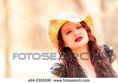 Stock Image - Portrait of a 33 year old brunette woman wearing a straw hat and looking at the camera, outdoors.. Fotosearch
