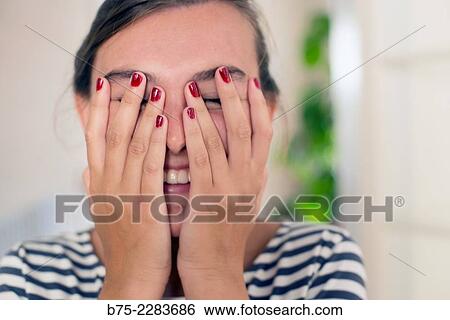 Stock Photograph - Portrait of young woman with her hands infront of the face smiling, happy and joy. Fotosearch