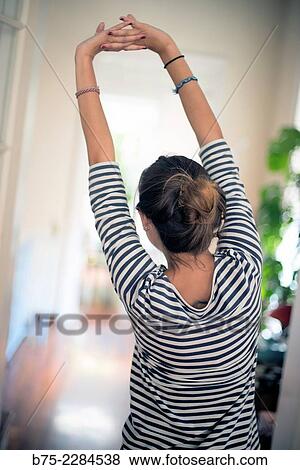 Stock Photo - Rear view of a young blonde woman standing, stretching his arms up.. Fotosearch