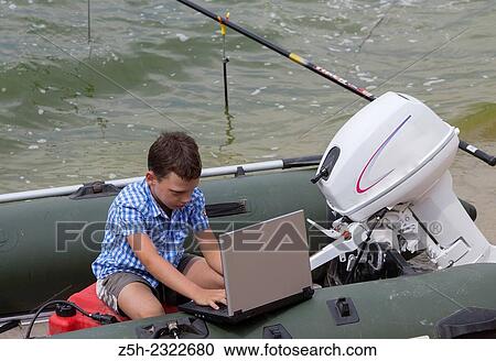 Stock Image - Teenager on a picnic by the river alone with a laptop.. Fotosearch