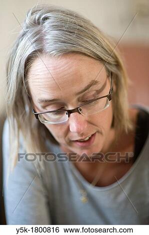 Stock Photograph - The Hague, Netherlands. Portrait of a middle-aged blonde woman with glasses in her living room. An portrait.. Fotosearch