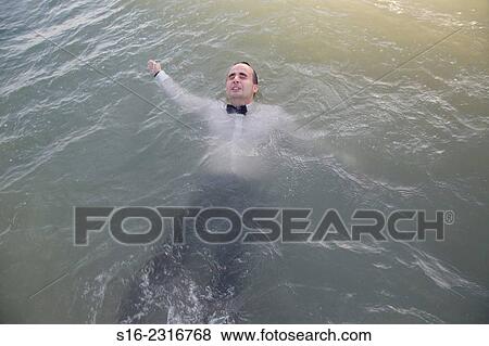 Stock Photo - Tired young man dressed up for party with white shirt and a bow-tie, swimming face up in the sea.. Fotosearch