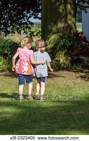 Two young friends girls walking through the grass with arm embracing back. Zawady Central Poland. View Large Photo Image Stock Photography - Two young friends girls walking through the grass with arm embracing back. Zawady Central Poland.. Fotosearch
