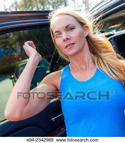 Stock Photo - 39 year old blond woman looking at the camera standing next to her car.. Fotosearch
