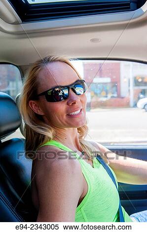 Stock Photography - 39 year old blond woman wearing fitness clothing driving a car and wearing sunglasses smiling at the camera.. Fotosearch