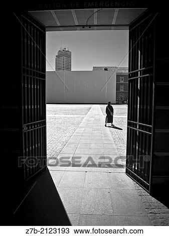 Stock Image - A woman walking in the courtyard of Conde Duque, Madrid, Spain.. Fotosearch