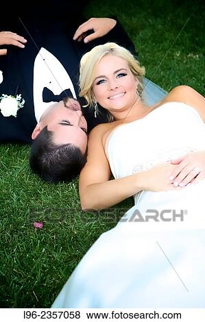 bride and groom laying on grass, enjoying the wedding day in her wedding dress and his tux View Large Photo Image Stock Photo - bride and groom laying on grass, enjoying the wedding day in her wedding dress and his tux. Fotosearch