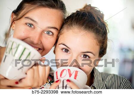 Close-up of two young girls with brown hair looking at the camera and holding in hands a cup of tea, with smiling and happy expression. View Large Photo Image Stock Photo - Close-up of two young girls with brown hair looking at the camera and holding in hands a cup of tea, with smiling and happy expression.. Fotosearch