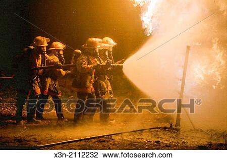 Group of firefighters holding hose spraying water on fire. View Large Photo Image Stock Image - Group of firefighters holding hose spraying water on fire.. Fotosearch