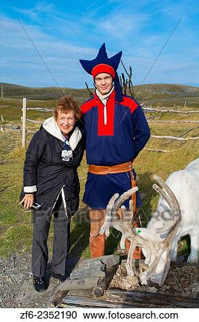 Stock Image - Honningsvag Norway cruise Hurtigruten Sami Tribal man in costume with reindeer and tourist woman at North Cape Northerm most place in Europe MR-25.. Fotosearch