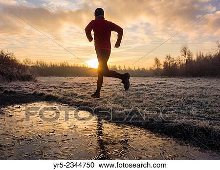 Stock Image - Man jogging on a frosty morning at sunrise near Billingham, North east England. United Kingdom.. Fotosearch