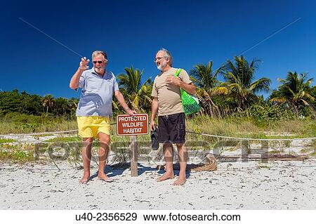 Stock Photo - Men standing by beach sign.. Fotosearch