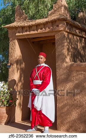 Stock Photograph - Morocco Atlas Mountains Boulmane Danes village man in red traditional costume portrait at doorway.. Fotosearch