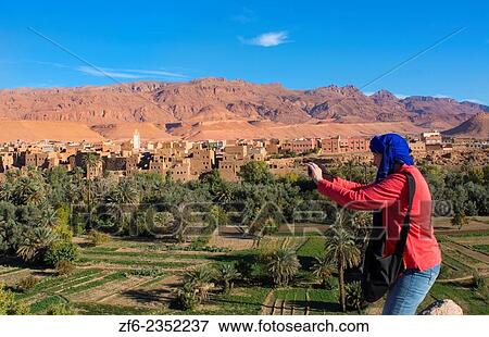 Morocco Atlas Mountains Tinghir Oasis and village with beautiful mountains and green palm trees and woman tourist taking photos. View Large Photo Image Stock Photo - Morocco Atlas Mountains Tinghir Oasis and village with beautiful mountains and green palm trees and woman tourist taking photos.. Fotosearch