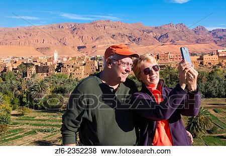 Stock Photo - Morocco Atlas Mountains Tinghir Oasis and village with beautiful mountains and green palm trees and tourist taking photos selfie.. Fotosearch