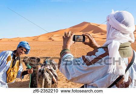Morocco Sahara Desert sand dunes in Las Palmeras area with local man taking cell phone phoyo of his friend and camel and peaks and sand. View Large Photo Image Stock Image - Morocco Sahara Desert sand dunes in Las Palmeras area with local man taking cell phone phoyo of his friend and camel and peaks and sand.. Fotosearch