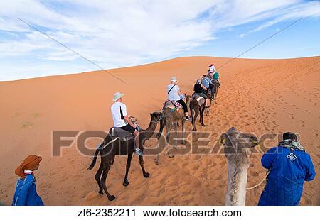 Stock Image - Morocco Sahara Desert sand dunes in Las Palmeras area with tourists riding camels on peaks and sand.. Fotosearch