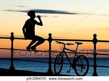Stock Image - Mountain biker watching the sun rise at Seaton Carew on the North east coast of England. United Kingdom.. Fotosearch