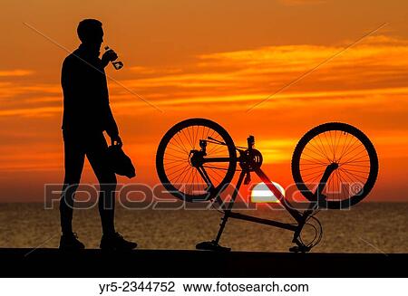 Stock Image - Mountain biker watching the sun rise at Seaton Carew on the North east coast of England. United Kingdom.. Fotosearch