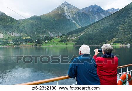 Stock Image - Norway cruise Hurtigruten ship fjord woman taking photo of scenic from balcony with old Norway Postal flag in Hjorundjorden MR-11.. Fotosearch