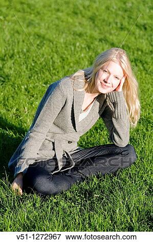 Stock Photo - Portrait of a young woman sitting in the park and smiling at camera. Fotosearch