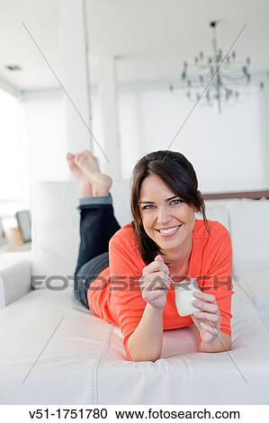 Stock Image - Pretty brunette woman enjoying a yogurt at the sofa. Fotosearch