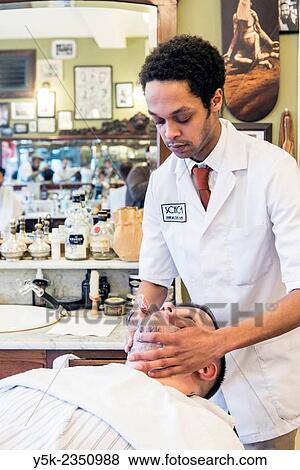 Stock Photo - Rotterdam, Netherlands. Barber store Schorem. Male customer lying back in his barber chair while receiving a wet shave.. Fotosearch