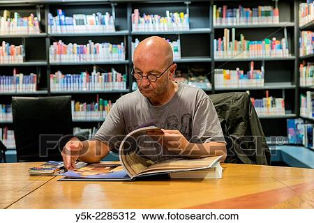Stock Image - Rotterdam, Netherlands. Middle aged man reading travel books in the city's public library.. Fotosearch