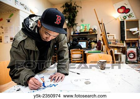 Rotterdam, Netherlands. North African artist, wearing a winter coat and cap, working on a sketch on the main production table of Via Kunst Studio's. View Large Photo Image Picture - Rotterdam, Netherlands. North African artist, wearing a winter coat and cap, working on a sketch on the main production table of Via Kunst Studio's.. Fotosearch