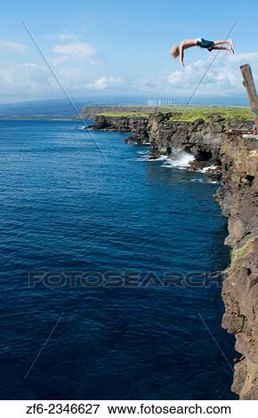 Stock Photo - South Point Hawaii Big Island cliff pole young man diving intp water danger dangerous dive water MR-2.. Fotosearch