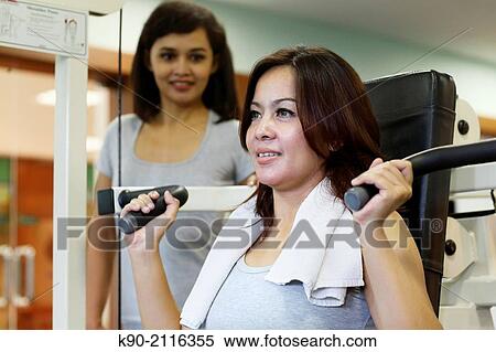 Stock Photography - Two asian women doing weightlifting at a machine, Jakarta, Indonesia, Southeast Asia.. Fotosearch